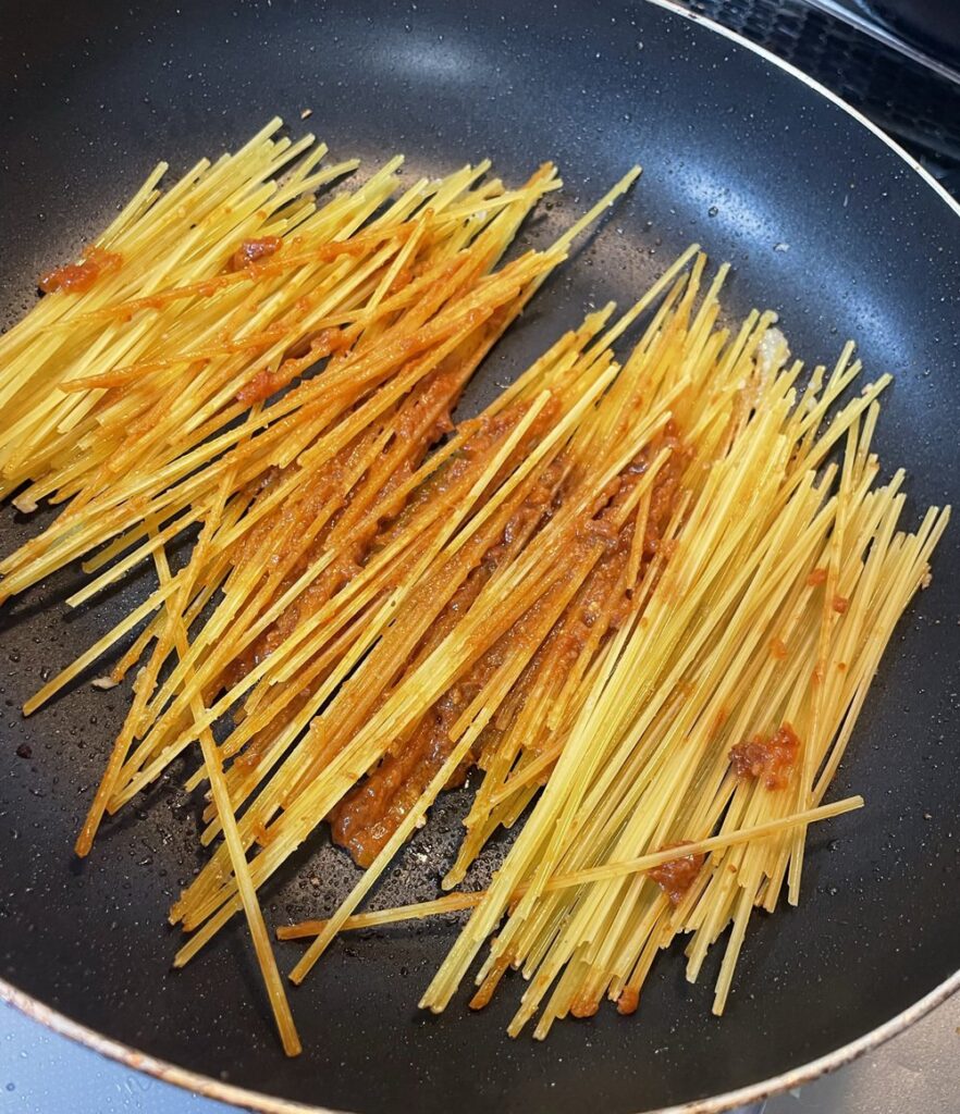 フライパンに半部に折ったスパゲティとハインツのボロネーゼソースを投入した様子