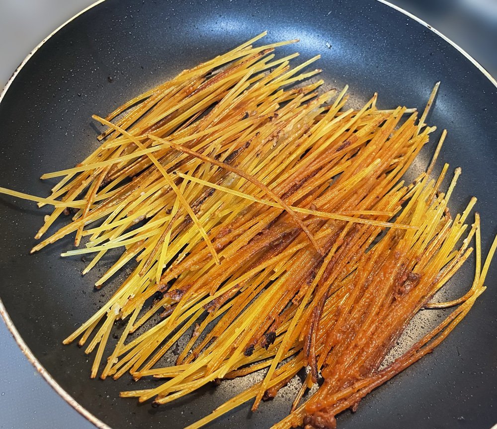 フライパンに投入したパスタが、ボロネーゼと絡み合って焦げ始めた様子