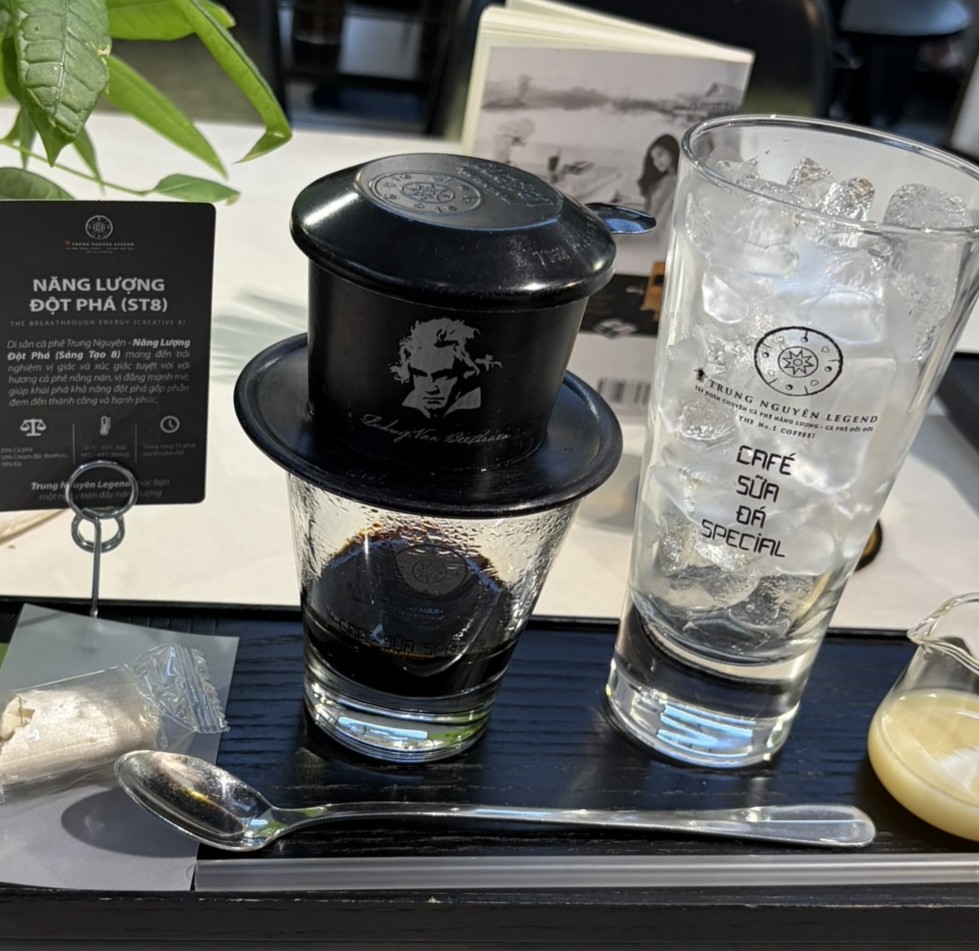 ベトナム現地のカフェ。ステンレス製のフィルター「フィン」から、グラスへゆっくりとコーヒーが滴る様子。横にはたっぷり氷が入ったグラスと練乳の入ったピッチャーが置かれている。