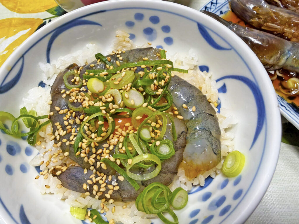 白ごはんの上に、タレに漬け込んだ「天使の海老」のカンジャンセウをのせ、中央に卵黄、たっぷりの刻みネギと白ごまをトッピングした贅沢な丼。